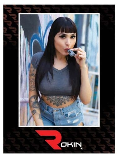 A woman with dark hair and tattoos on her arms and torso holds a gray vape to her mouth; "ROKIN" is at the bottom.