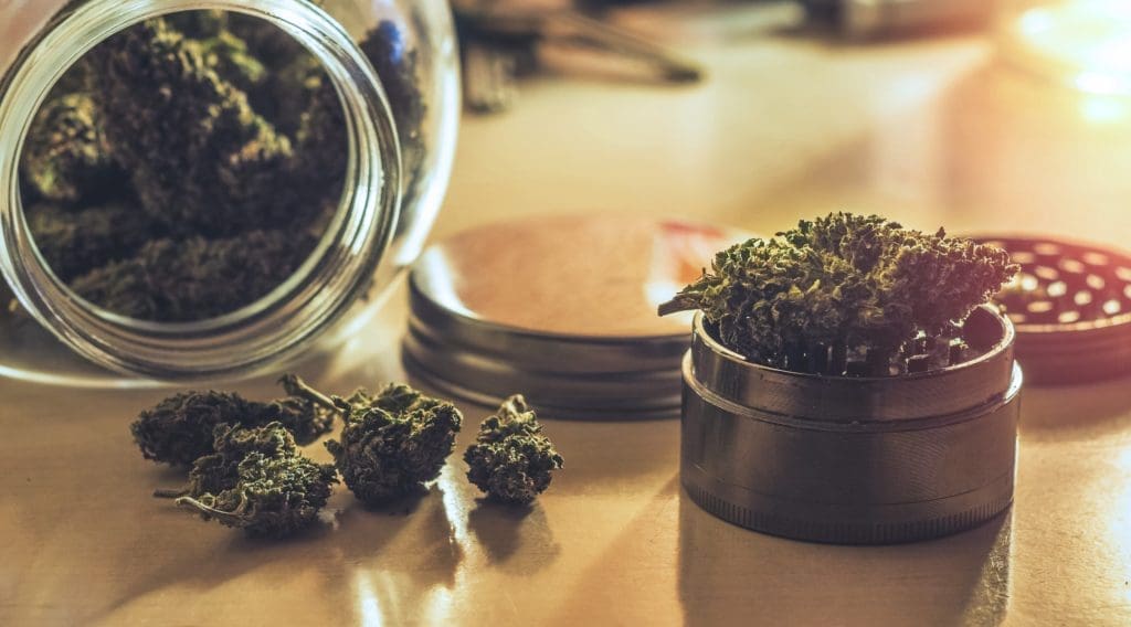 Cannabis,Flower,Buds,In,Glass,Jar,And,Grinder,On,Table Jar of cannabis on the table