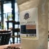 Mushroom Head Coffee 2 A bag of "Organic Coffee with functional mushrooms" stands on a wooden table next to a pile of coffee beans.