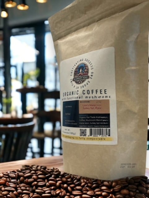 Mushroom Head Coffee 2 A bag of "Organic Coffee with functional mushrooms" stands on a wooden table next to a pile of coffee beans.